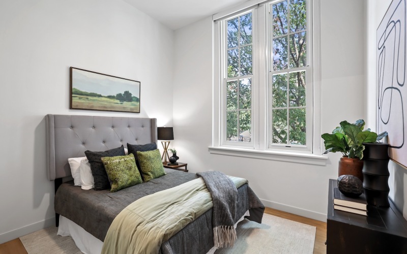 bedroom with a large window and a bed with a dresser in front of it